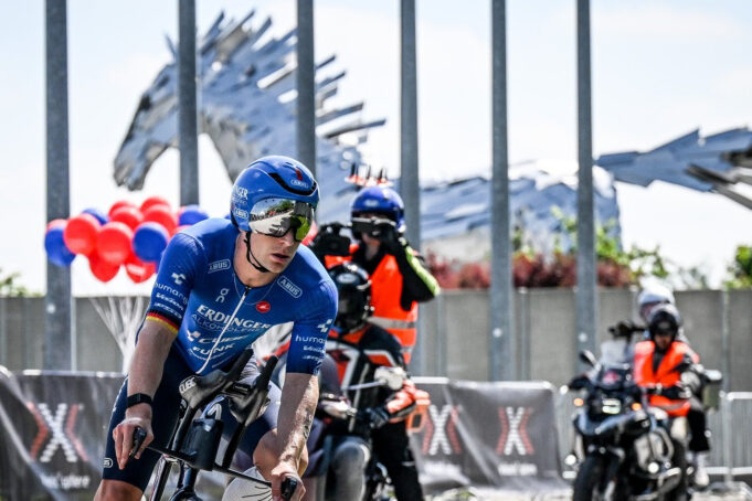 A triathlete on a bike with two support motorbikes behind hm
