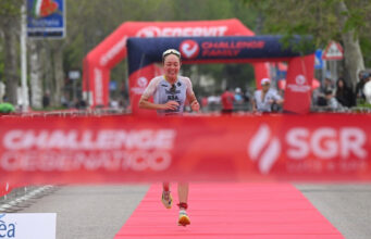 Female triathlete runs towards a red finish tape