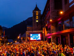 Trail 100 Andorra by UTMB® Preview A mass of runners wait at the start line at night in front of a TV screen and a lit church tower