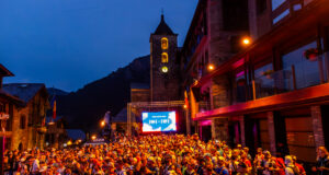 A mass of runners wait at the start line at night in front of a TV screen and a lit church tower