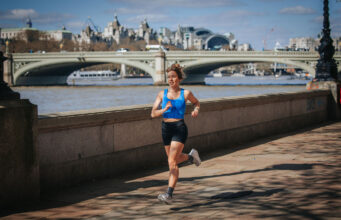 Woman in black shorts and blue crop top runs by the River Thames in central London