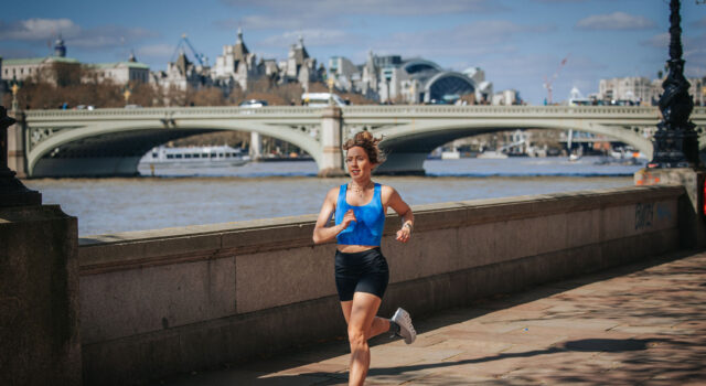Woman in black shorts and blue crop top runs by the River Thames in central London