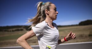 Woman in white tshirt running along a road in what looks like a hot, sparse landscape. She's carrying a SiS gel