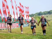 Group of four women finish a trail race holding hands and smiling