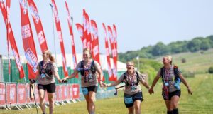 Group of four women finish a trail race holding hands and smiling