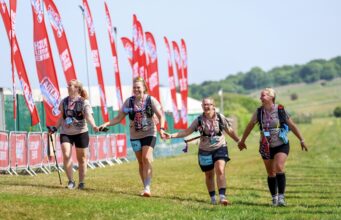 Group of four women finish a trail race holding hands and smiling