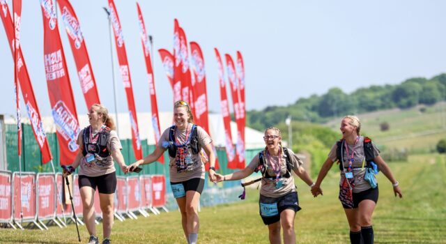 Group of four women finish a trail race holding hands and smiling