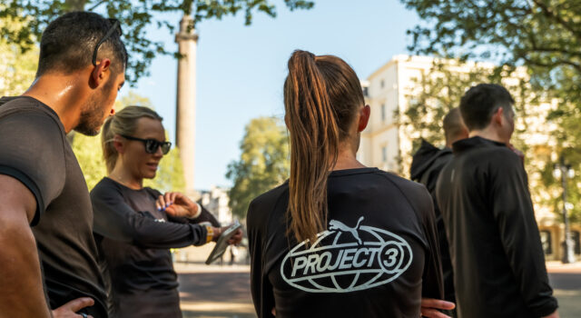 A group of people wearing black PUMA tshirts congregate on a street