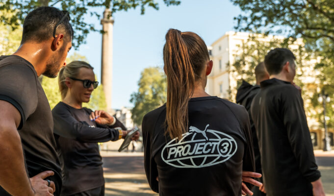 A group of people wearing black PUMA tshirts congregate on a street