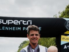 Jonny Brownlee stands at the finish line with a medal around his neck, holding his baby