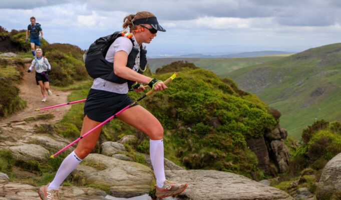 Summer Spine Race 2026: course records fall A woman wearing shorts, tshirt, race pack and carrying poles traverses rocky slabs.