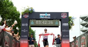 Male triathlete runs under finish gantry holding red tape