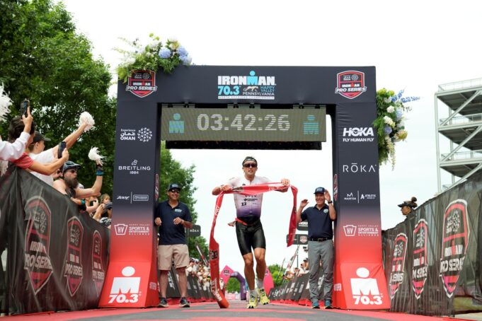 Trevor Foley captured North American Championship title and maximum Experience Oman IRONMAN Pro Series points in State College, Pa credit Patrick McDermott Getty Images for IRONMAN Male triathlete runs under finish gantry holding red tape