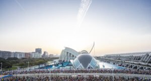 Masses of runners on a road in front of a very futuristic looking white and blue building