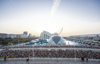 Realbuzz partners with Valencia Marathon Masses of runners on a road in front of a very futuristic looking white and blue building