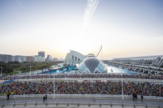 Masses of runners on a road in front of a very futuristic looking white and blue building