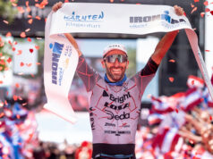 Mattia Ceccarelli (ITA) Takes His First Professional IRONMAN Win at IRONMAN Kärnten-Klagenfurt, Austria Male triathlete in sunglasses liftes finish tape above head as confetti falls around him.