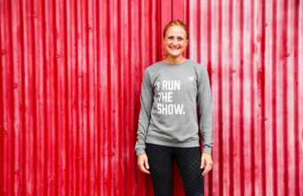 Mel Bound awarded OBE for women’s community sport Smiling woman in front of red background, wearing grey sweatshirt saying I RUN THE SHOW