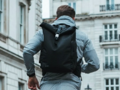 A man runs through a city past white buildings wearing a backpack
