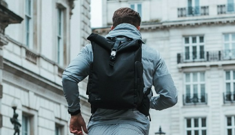 A man runs through a city past white buildings wearing a backpack