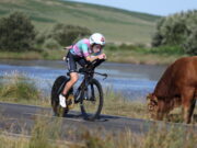Palmer and Rayner win IRONMAN 70.3 Swansea Woman on bike cycles near lake past brown cow