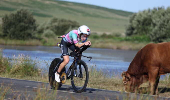 Palmer and Rayner win IRONMAN 70.3 Swansea Woman on bike cycles near lake past brown cow