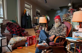7 Things Every Runner Can Learn from Lazarus Lake An elderly man wering running shoes, jeans, plaid shirt and red beany hat sits in an armchair in a room full of stuff