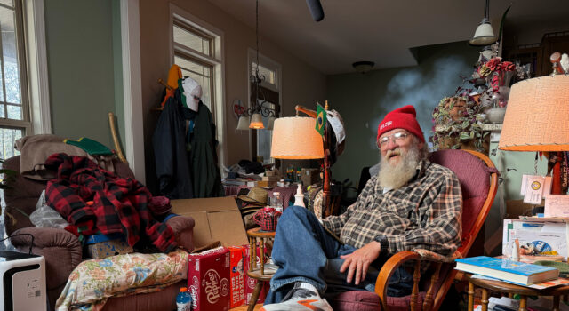 7 Things Every Runner Can Learn from Lazarus Lake An elderly man wering running shoes, jeans, plaid shirt and red beany hat sits in an armchair in a room full of stuff