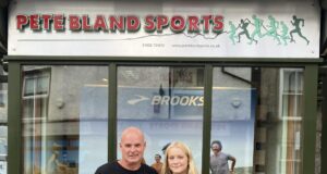 A man and young woman stand in front of a shop front with Pete Bland Sports on the sign
