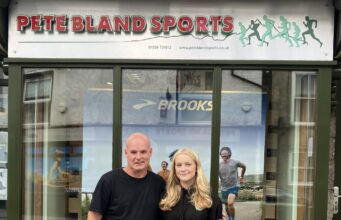 Cumbria’s rising fell runners awarded bursary A man and young woman stand in front of a shop front with Pete Bland Sports on the sign