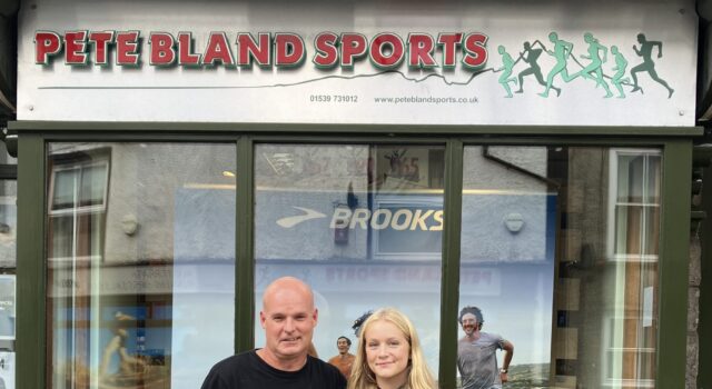Cumbria’s rising fell runners awarded bursary A man and young woman stand in front of a shop front with Pete Bland Sports on the sign