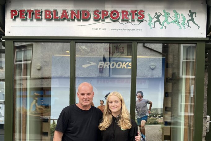 A man and young woman stand in front of a shop front with Pete Bland Sports on the sign