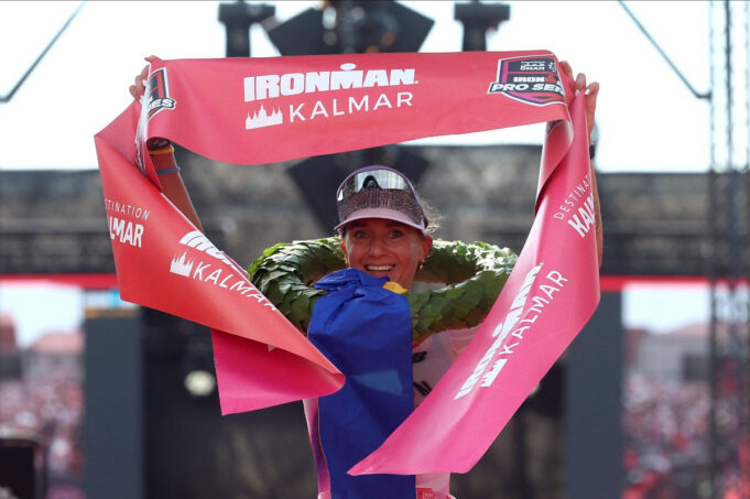 Ironman Laura Phillip Female triathlete grasps red finish tape above her head