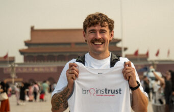 Jack Jarvis to run 13,000km from Beijing to London Smiling man in white tshirt and black shorts holds a brainstrust white vest. He stands in front of a Chinese temple