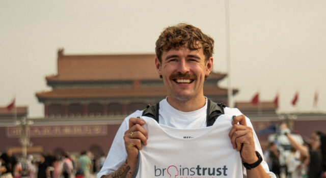 Jack Jarvis to run 13,000km from Beijing to London Smiling man in white tshirt and black shorts holds a brainstrust white vest. He stands in front of a Chinese temple