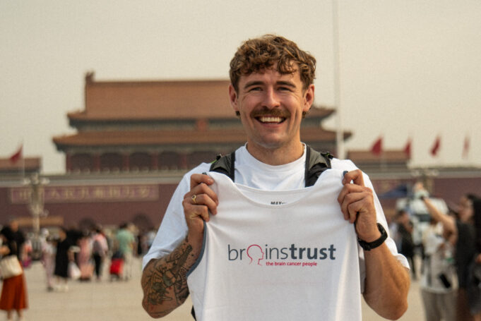 Jack Jarvis sets off on world record 13,000km run for brainstrust - pictured at start line in Beijing Smiling man in white tshirt and black shorts holds a brainstrust white vest. He stands in front of a Chinese temple