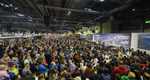 Hundreds of people sit in front of a large stage listening to a speaker