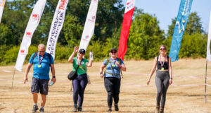 4 people walk across a field lined with colourful advertising flags