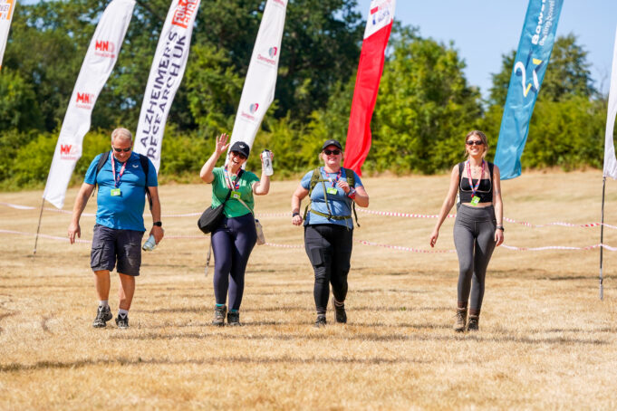 North Downs Ultra Challenge Surrey Hills 4 people walk across a field lined with colourful advertising flags
