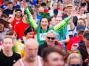 Race Guide: Wizz Air Ealing Half Marathon 2026 Lady in green in the middle of a crowd of runners. She has her arms outstretched and looks overjoyed to be there.