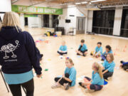 100km to support young people’s mental health A group of primary age children wearing blue tshirts sit in a circle on a wooden floor while a lady standing next to a flipchart explains something to them