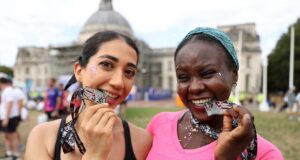 Two women smile while biting their running medals