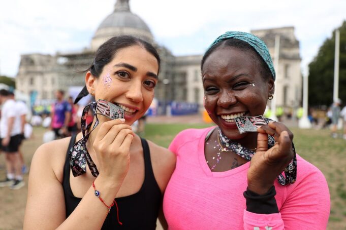 Two women smile while biting their running medals