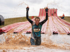 A very muddy runner splashes through a muddy thigh deep puddle at the bottom of an inflatable slide