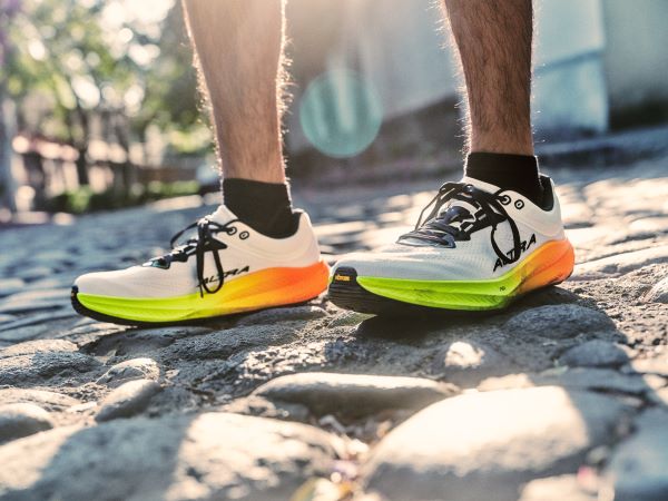 F26_Road_Torin9_M_Wht_Blk_Ylw_AL0A85TN87A_4421 Feet and lower legs of a man, wearing road shoes.