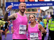 Dublin Marathon Group and Official Charity Partner realbuzz Launch New Marathon Weekend Shakeout Run A man and woman wearing pink running vvests pose n front of a Dublin marathon gantry