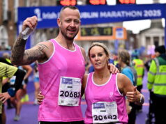 Dublin Marathon Group and Official Charity Partner realbuzz Launch New Marathon Weekend Shakeout Run A man and woman wearing pink running vvests pose n front of a Dublin marathon gantry