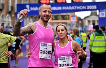 A man and woman wearing pink running vvests pose n front of a Dublin marathon gantry