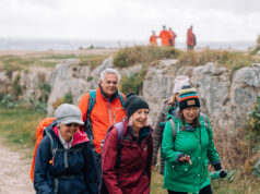 OutdoorXpo welcomes The Ramblers as hiking partner 4 people of the older variety in hiking gear walk past a stone outcrop.