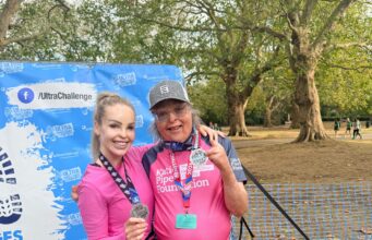 A man and woman pose in pink tshirts with medals